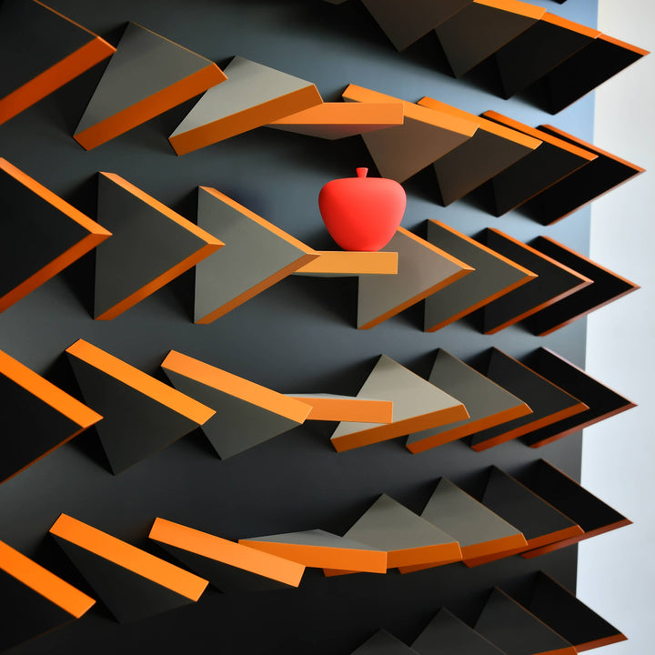 Red apple on a geometric shelf design with orange and gray shapes.