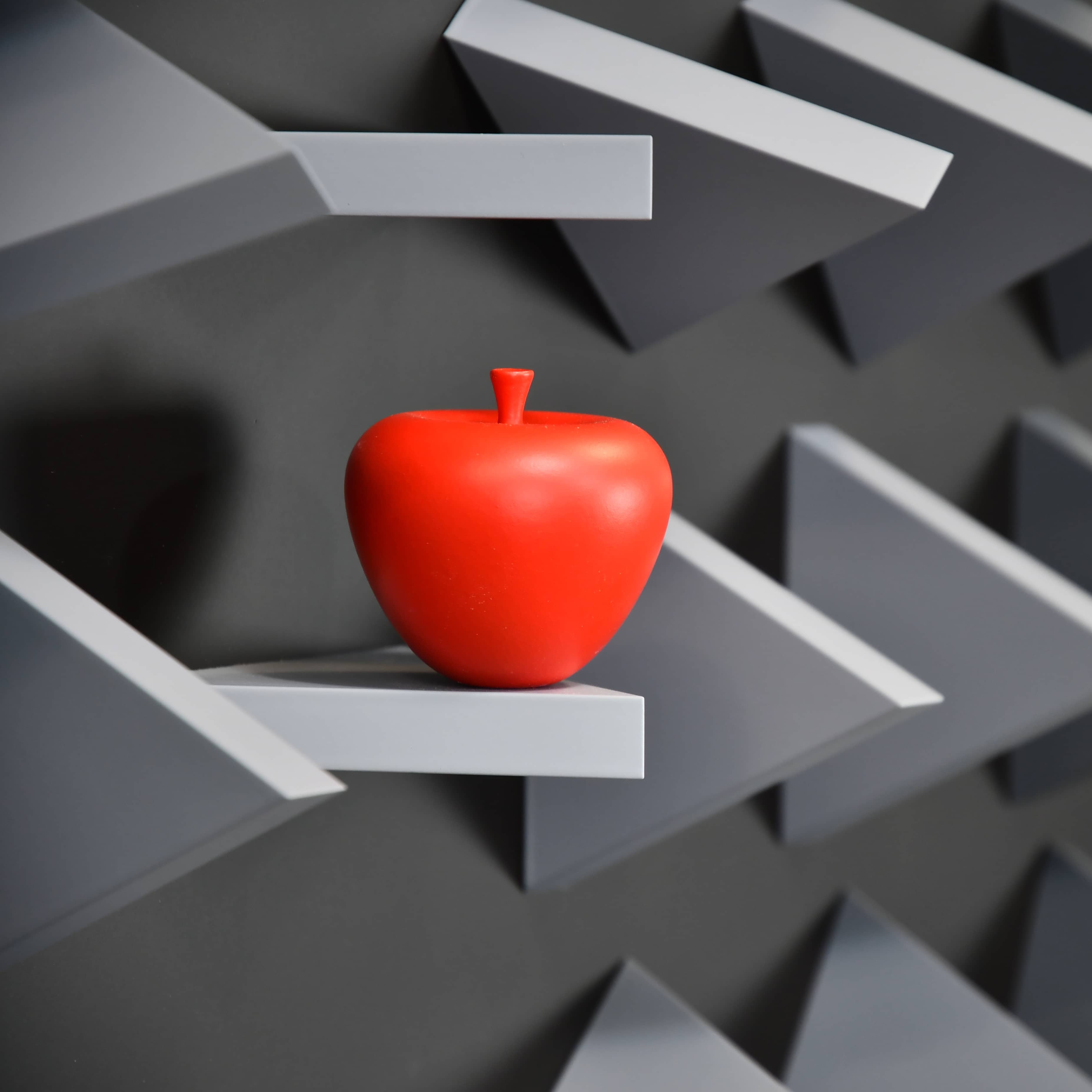 Red apple on a geometric gray shelf against a black and white background